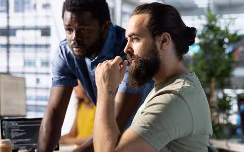 Two ethical hackers review code on a monitor.