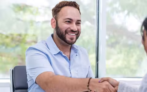 A career counselor seated at a desk shakes hands with a client.