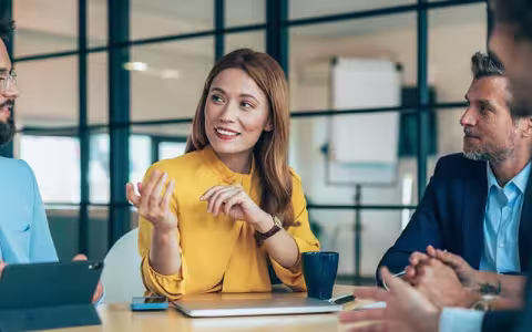 A group of colleagues talking as they sit at a conference table.
