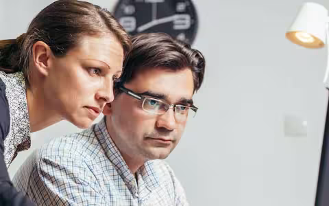 Two cybersecurity analysts in an office review an issue.