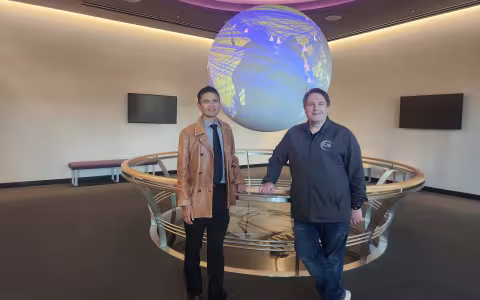 CEHC's Ariel Pinto and Center for Internet Security's Sean Atkinson stand in front of the Science on a Sphere globe at ETEC.