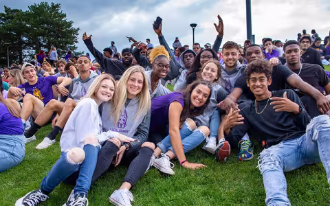 Students sitting in the grass together at Homecoming.
