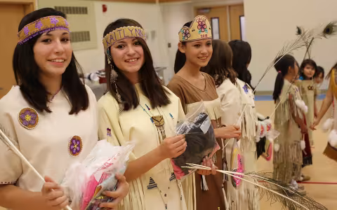 A group of Alaska Native young women and girls perform a traditional cultural dance in a gym wearing traditional attire.