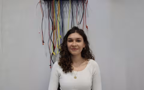 A smiling Marianna Karagiannas stands in front of a white wall adorned with dangling electrical cords. 
