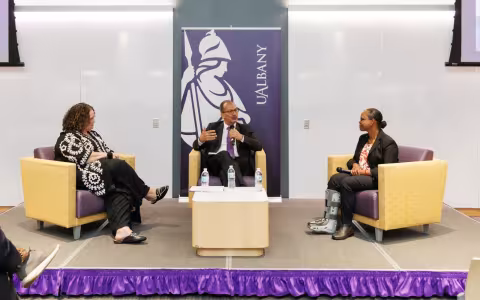Dr. Havidan Rodriguez, Dr. Tamarra James-Todd, and Johanne Morne sit in chairs on a stage.