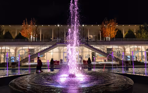 The fountains at Campus Center at night are lit up in purple light.