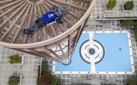 UAlbany Mascot Damien reclines with his legs crossed and arms behind his head on top of the Carillon.
