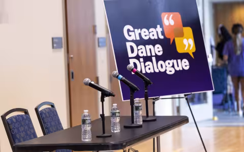 An empty table with microphones and a sign to the right of the table that says Great Dane Dialog.