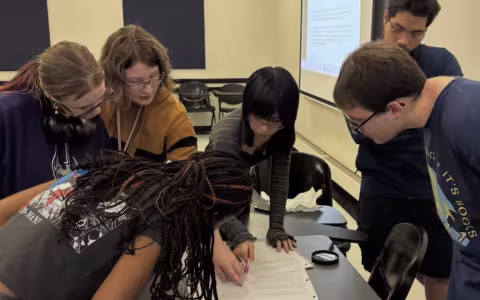 Students huddle around paperwork on a desk