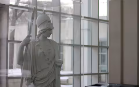 A statue of Minerva stands in the Science Library atrium. Glass windows are behind her.