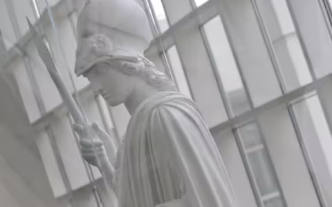 A white statue of Minerva stands in the Science Library atrium. Glass windows are behind her.