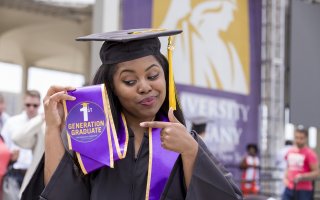 New graduate enthusiastically points at her first generation badge during UAlbany's undergraduate commencement ceremony.