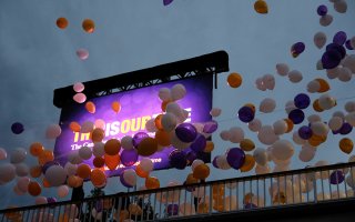 Balloons soar before a large video screen