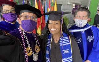 A Class of 2021 graduate takes a selfie on stage with President Havidán Rodríguez, SUNY Chancellor Jim Malatras and School of Business Dean Nilanjan Sen.