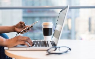 Woman browses laptop and smartphone during remote meeting.