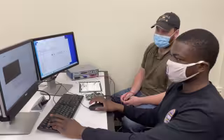 Two college students in facemasks work together on a computer
