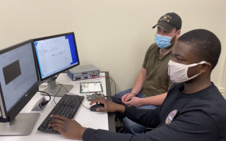 Two college students in facemasks work together on a computer