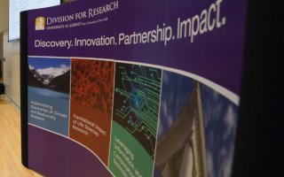 A curved, purple sign with the heading Division of Research displays images and graphics depicting different fields of study
