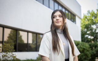 Student Cassie Kane stands in front of the School of Public Health, looking to the side.