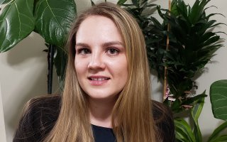 Portrait of Tatyana Tarasevich, wearing black. Plants can be seen in the background.