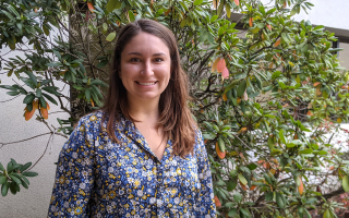 Taylor Perre, wearing a blue and yellow floral shirt, poses for a portrait photograph in front of shrubbery.