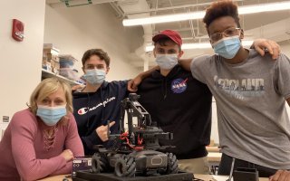 Marcie Fraser and three students in the EPICH program stand in front of a robot inside CEHC's makerspace at ETEC. 