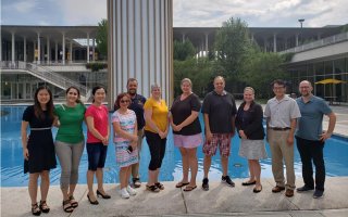 A group of 11 adult men and women stand in front of the main fountain pond.