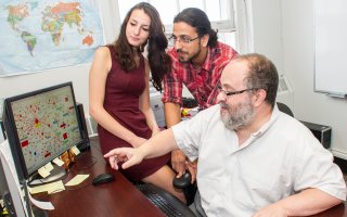 Jona Hoxha, and Alejandro Castro-Reina, with UAlbany Professor Victor Asal review a chart on a computer indoors.