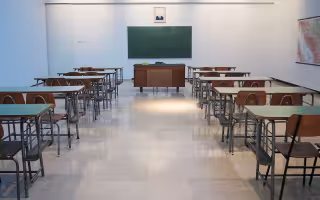 Ana empty classroom with two rows of student desks and chairs and a teacher's desk in front