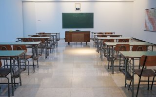 Ana empty classroom with two rows of student desks and chairs and a teacher's desk in front