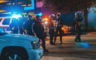 Police in riot gear stand amid cars on a street lit by headlights