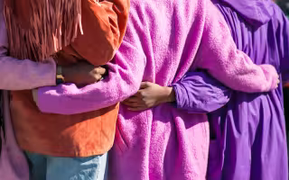 A group of diverse women embrace while standing outside.