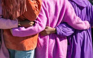 A group of diverse women embrace while standing outside.
