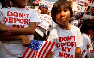 A young boy stands in front of a crowd of children, all wearing Don't Deport My Mom teeshirts.