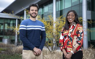 A young man and young woman stand beside each other, smiling, in the courtyard of the Life Sciences Research Building