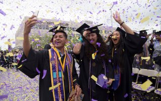 New UAlbany graduates celebrate amidst a sea of purple and gold confetti.