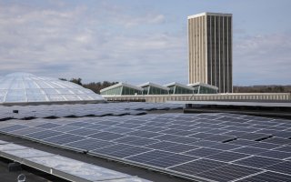 Solar panels cover a rooftop at UAlbany, with a residential tower in the background