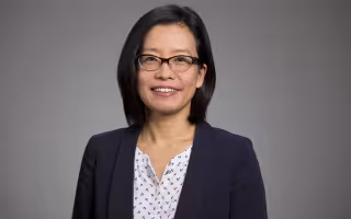 UAlbany School of Business Associate Professor Na Dai portrait - a woman wears glasses and a blue jacket.