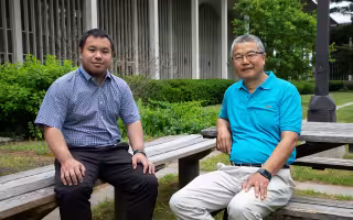 A young Chinese man and an elder Chinese man on benches in UAlbany courtyard