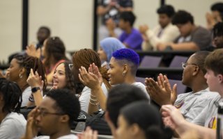 Students seated together in a lecture hall smile and applaud