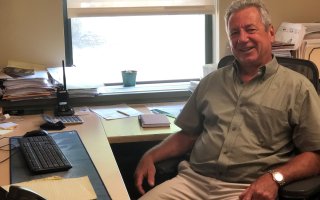 Michael Vadney, smiling, sits at his computer desk in his office