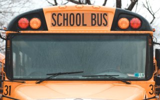 A close-up image of a yellow school bus with a rain-streaked windshield surrounded by other buses.