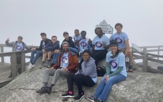 UAlbany weather camp students and faculty leaders sit on rocks atop the Whiteface Mountain summit..