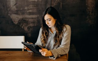 A woman with long brown hair works on a tablet while seated.