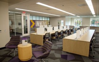 An indoor office with rows of tables and chairs with a large sign that says Innovate on the back wall.