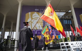 A photo of student flagbearers in graduation robes carrying various international flags onto the stage at Commencement.