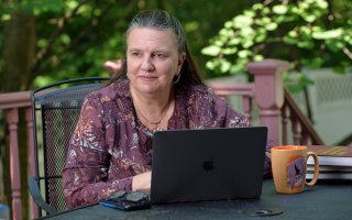 CEAS Dean Michele J. Grimm sits at a table outdoors with a laptop in front of her and a coffee mug.