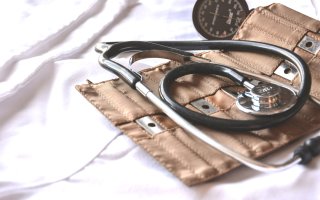 Black and silver stethoscope laid atop a brown blood pressure cuff. Instruments are arranged on a white cloth. 