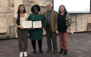 Four smiling people stand in a row, two holding certificates