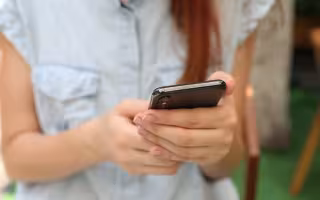 Woman in blue button down shirt holds her cell phone.